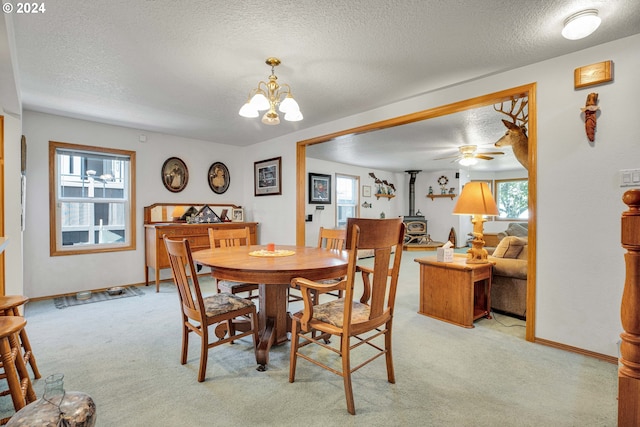 dining room featuring light colored carpet, a textured ceiling, ceiling fan with notable chandelier, and a wood stove