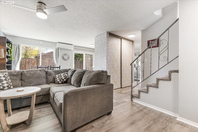 living room with an AC wall unit, ceiling fan, light hardwood / wood-style flooring, and a textured ceiling