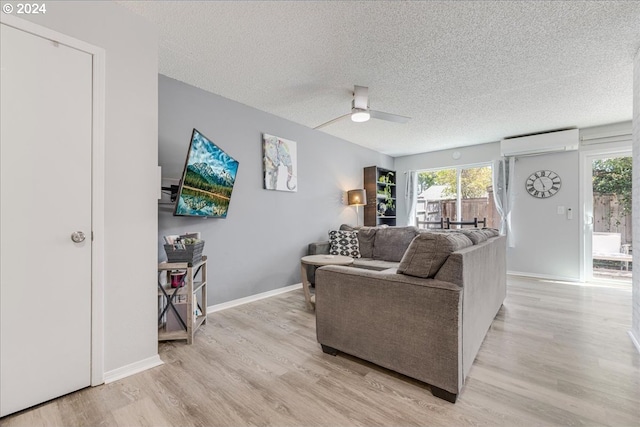 living room featuring ceiling fan, a wall mounted AC, light wood-type flooring, and plenty of natural light