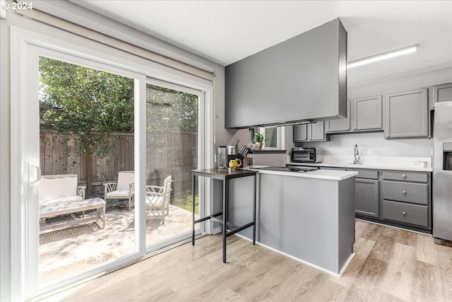 kitchen featuring kitchen peninsula, light hardwood / wood-style floors, gray cabinetry, and stainless steel fridge