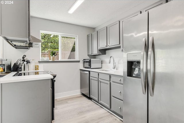 kitchen featuring stainless steel appliances, sink, a textured ceiling, light hardwood / wood-style floors, and gray cabinetry