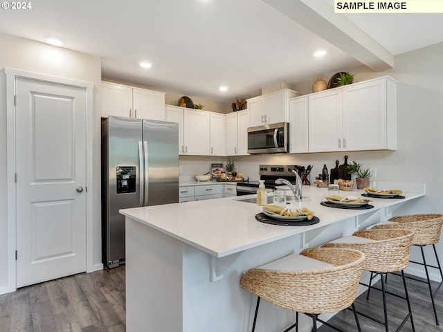 kitchen featuring kitchen peninsula, appliances with stainless steel finishes, dark hardwood / wood-style flooring, a kitchen breakfast bar, and white cabinets