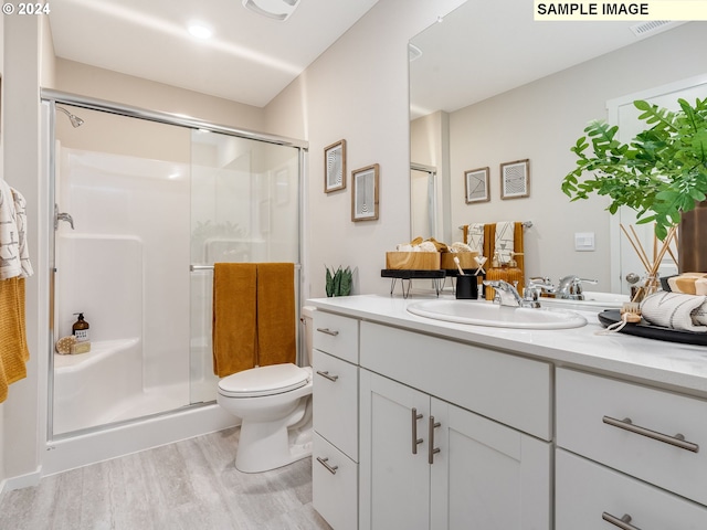 bathroom with hardwood / wood-style floors, vanity, toilet, and a shower with shower door