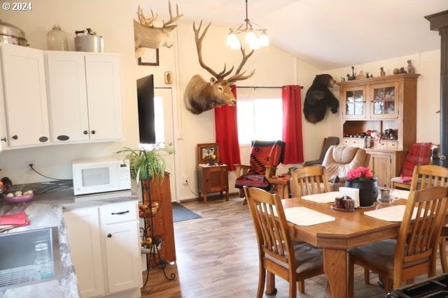 dining area with vaulted ceiling, a notable chandelier, and light wood-type flooring