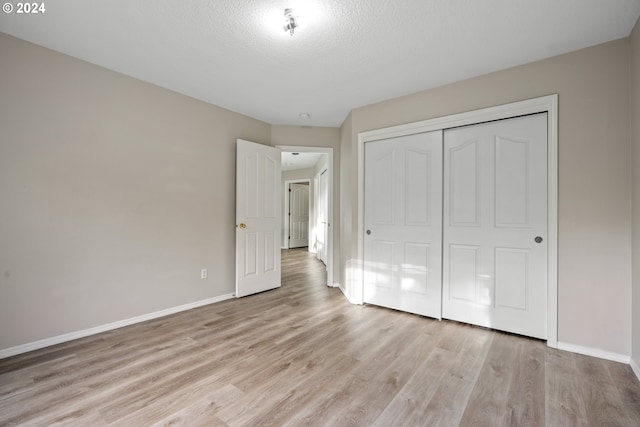 unfurnished bedroom with a textured ceiling, light hardwood / wood-style floors, and a closet