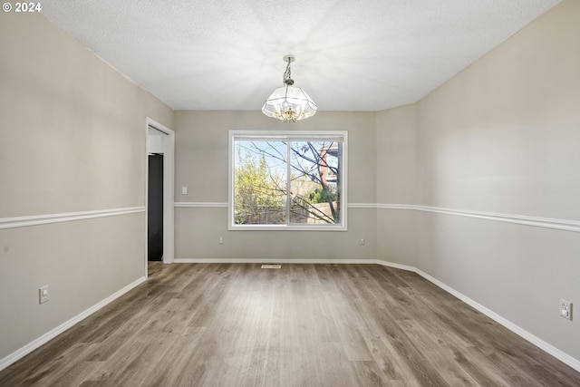 unfurnished dining area with wood-type flooring, a textured ceiling, and a chandelier