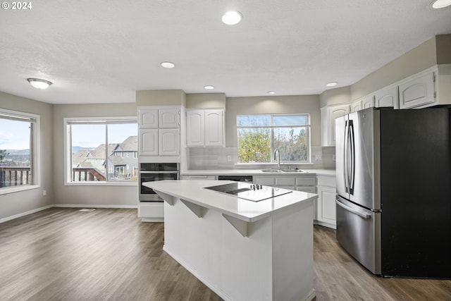 kitchen featuring black appliances, plenty of natural light, a kitchen island, and white cabinets