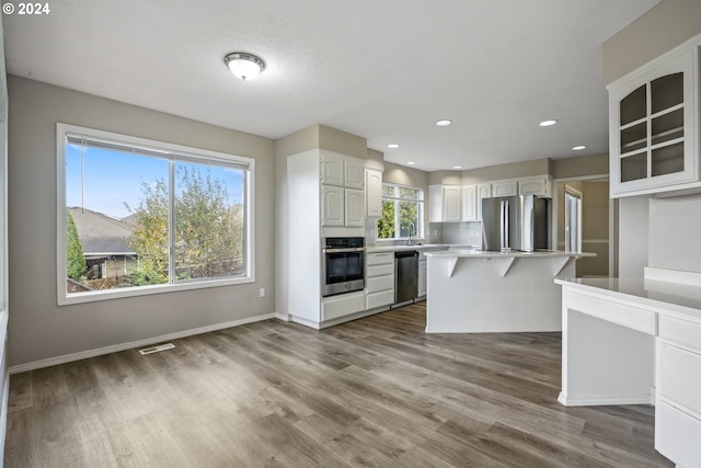 kitchen with a breakfast bar, appliances with stainless steel finishes, white cabinets, and a healthy amount of sunlight