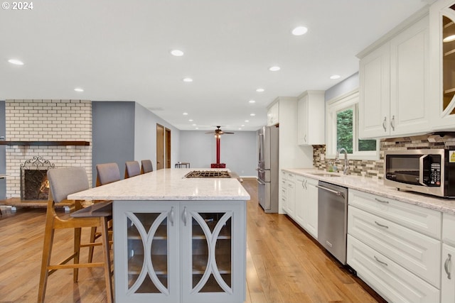 kitchen with stainless steel appliances, light stone counters, a kitchen bar, light hardwood / wood-style flooring, and a center island