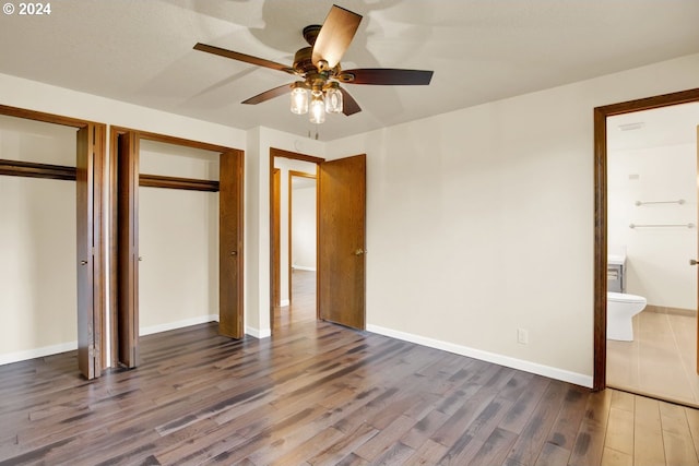 unfurnished bedroom featuring ceiling fan, dark hardwood / wood-style floors, ensuite bath, and two closets