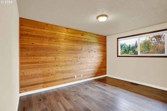 empty room featuring hardwood / wood-style floors, wooden walls, and a textured ceiling