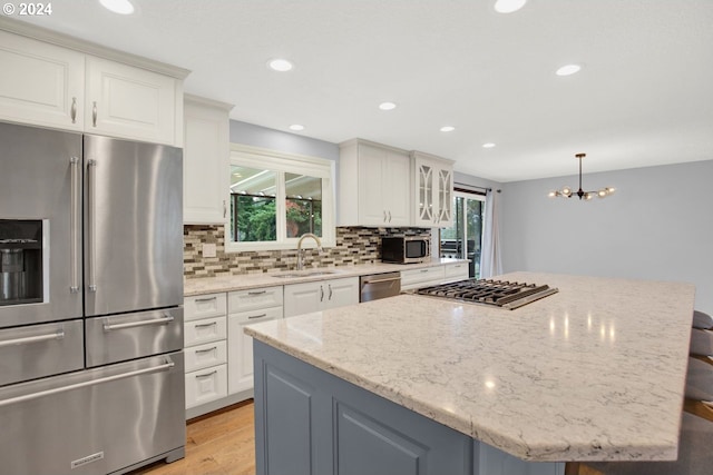 kitchen with white cabinetry, appliances with stainless steel finishes, light stone countertops, sink, and a center island