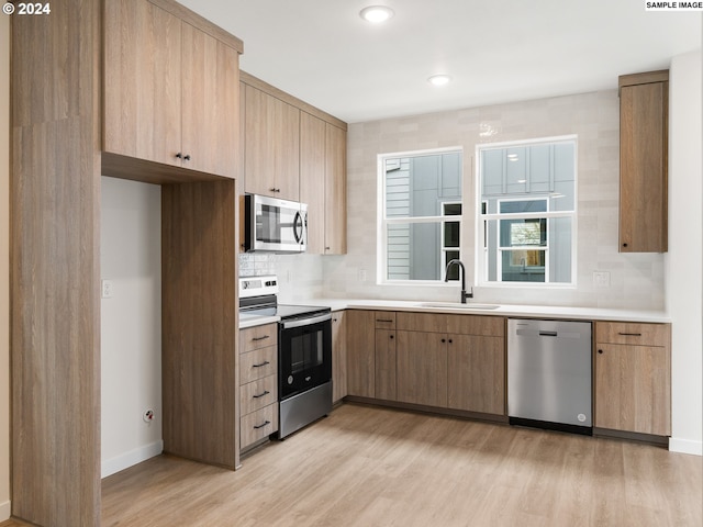 kitchen with backsplash, stainless steel appliances, light wood-type flooring, and sink