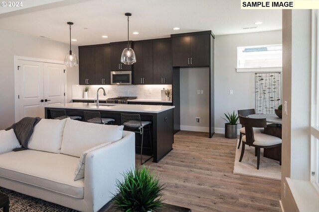 kitchen with wood-type flooring, a kitchen island with sink, stainless steel appliances, and backsplash