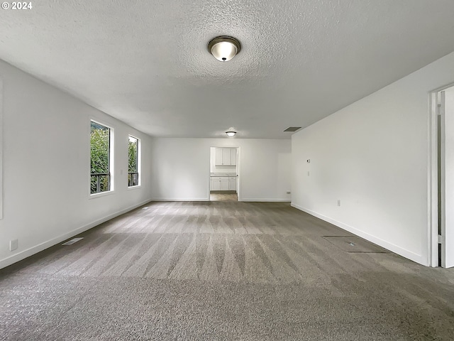 spare room with a textured ceiling and dark colored carpet