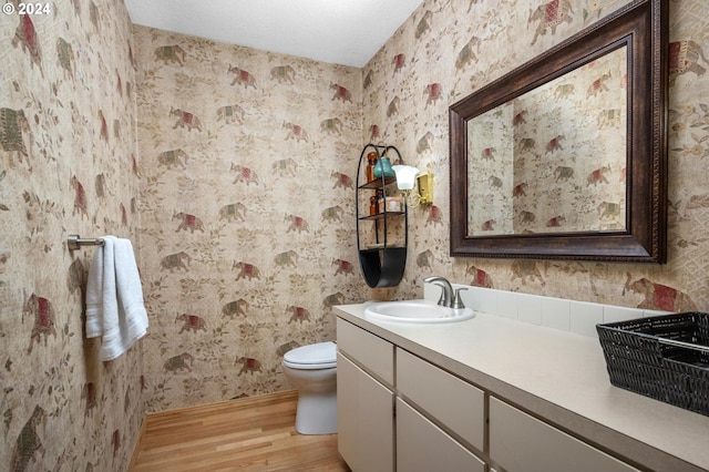 bathroom featuring wood finished floors, vanity, baseboards, toilet, and wallpapered walls