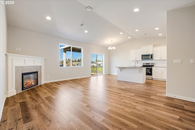 unfurnished living room with a tiled fireplace, lofted ceiling, light hardwood / wood-style floors, and sink