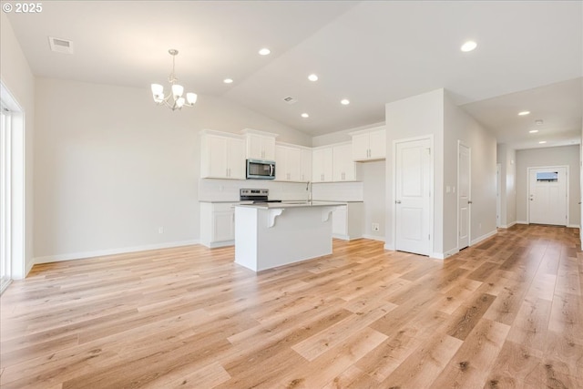 kitchen with white cabinetry, an island with sink, a notable chandelier, stainless steel appliances, and light hardwood / wood-style floors