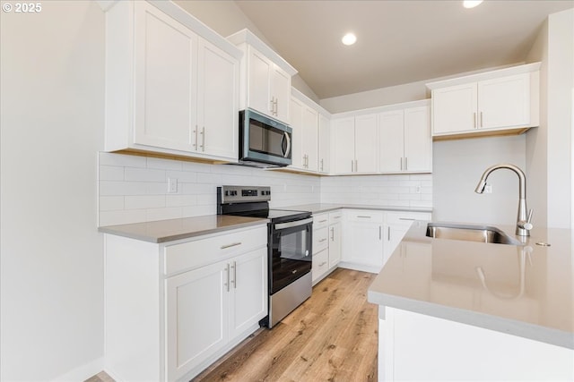 kitchen with sink, white cabinetry, light wood-type flooring, appliances with stainless steel finishes, and backsplash