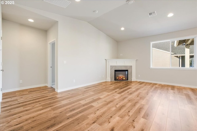 unfurnished living room featuring lofted ceiling, a tiled fireplace, and light hardwood / wood-style flooring