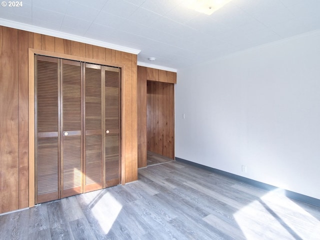 unfurnished bedroom featuring wood walls, a closet, light hardwood / wood-style flooring, and ornamental molding