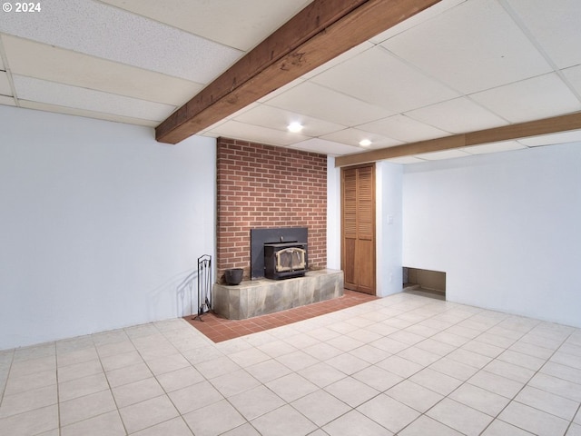 basement with a paneled ceiling, a wood stove, and light tile patterned flooring