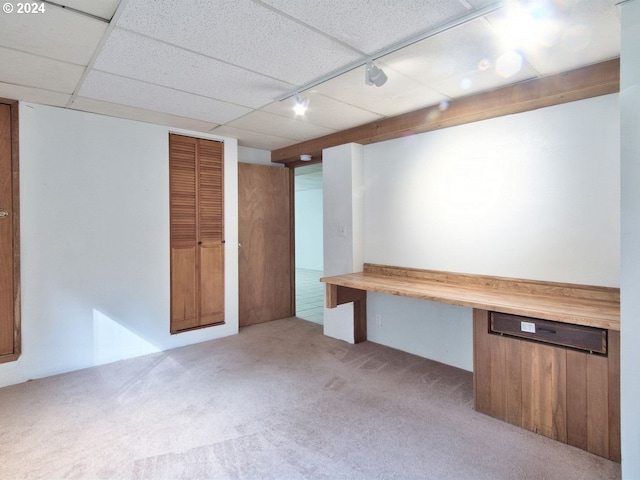 basement with built in desk, light carpet, and a drop ceiling