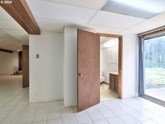 tiled spare room with a drop ceiling, a healthy amount of sunlight, and a brick fireplace