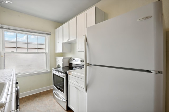 kitchen featuring stainless steel electric stove, white fridge, and white cabinetry