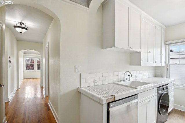 kitchen featuring tile countertops, sink, stainless steel dishwasher, white cabinetry, and washer / clothes dryer