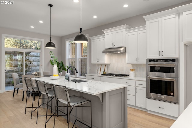 kitchen with sink, light hardwood / wood-style flooring, decorative light fixtures, a kitchen island with sink, and white cabinets