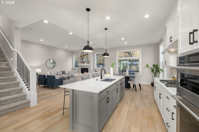 kitchen featuring white cabinets, sink, light wood-type flooring, and an island with sink