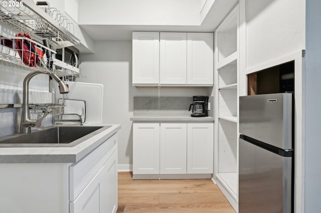 kitchen featuring white cabinetry, sink, stainless steel refrigerator, and light hardwood / wood-style flooring