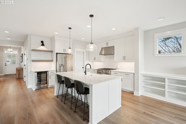 kitchen featuring white cabinetry, premium appliances, wine cooler, an island with sink, and decorative backsplash