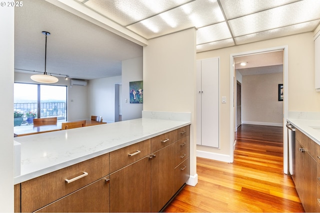 kitchen with brown cabinets, a wall mounted AC, light wood-style floors, light stone countertops, and baseboards