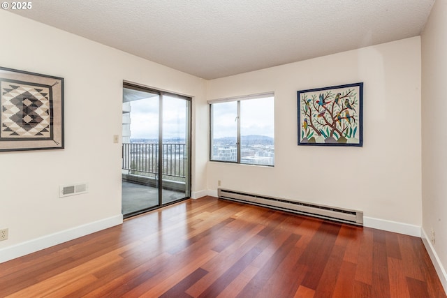 empty room with a baseboard radiator, visible vents, baseboards, and wood finished floors