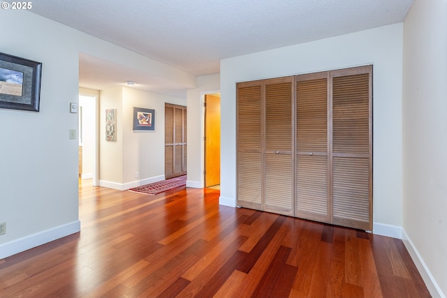 unfurnished bedroom with a closet, a textured ceiling, baseboards, and wood finished floors