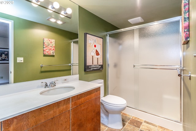 bathroom with stone finish floor, a stall shower, vanity, and toilet