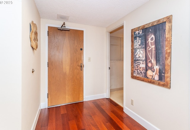 corridor featuring a textured ceiling, baseboards, and wood finished floors