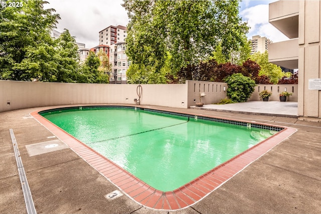 view of swimming pool featuring a fenced in pool, a patio area, fence, and a city view