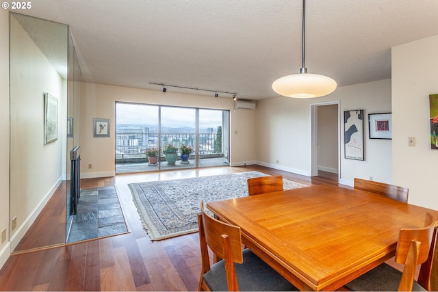 dining space featuring a textured ceiling, baseboards, wood finished floors, and a wall mounted air conditioner