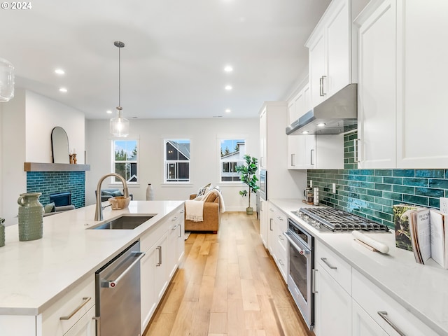 kitchen with appliances with stainless steel finishes, sink, light hardwood / wood-style floors, pendant lighting, and white cabinets