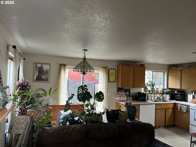 kitchen with a textured ceiling, white appliances, sink, and hanging light fixtures