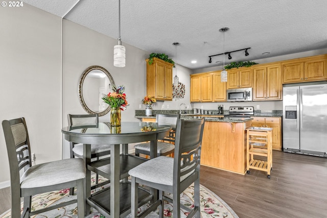 kitchen with dark wood-type flooring, hanging light fixtures, stainless steel appliances, a kitchen breakfast bar, and a textured ceiling