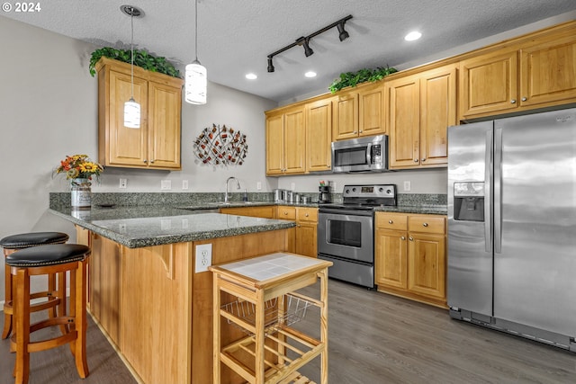 kitchen with appliances with stainless steel finishes, hanging light fixtures, a kitchen breakfast bar, dark hardwood / wood-style floors, and kitchen peninsula