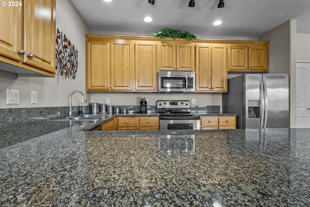 kitchen with sink, stainless steel appliances, dark stone counters, and a textured ceiling