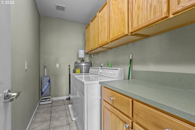 clothes washing area with cabinets, washer and clothes dryer, secured water heater, and light tile patterned floors