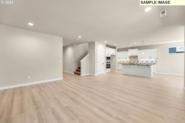 unfurnished living room with a textured ceiling and light hardwood / wood-style floors