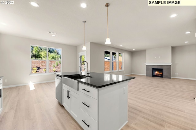 kitchen featuring a kitchen island with sink, sink, a tiled fireplace, light hardwood / wood-style flooring, and decorative light fixtures