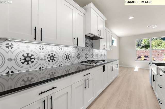 kitchen featuring white cabinets, stainless steel gas cooktop, backsplash, dark stone counters, and light hardwood / wood-style floors